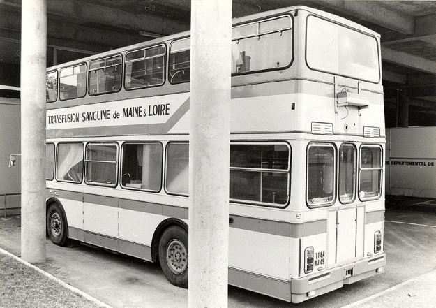 Photo noir et blanc d'un bus historique à 2 étages de l'EFS pour les collectes mobiles du don du sang en Maine-et-Loire des années 70-80, sous un hangar.